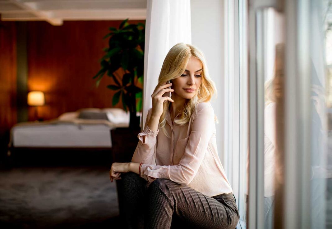 pretty-young-blonde-woman-with-mobile-phone-by-window-room ŽENA PRICA NA MOBITEL POKRAJ PROZORA