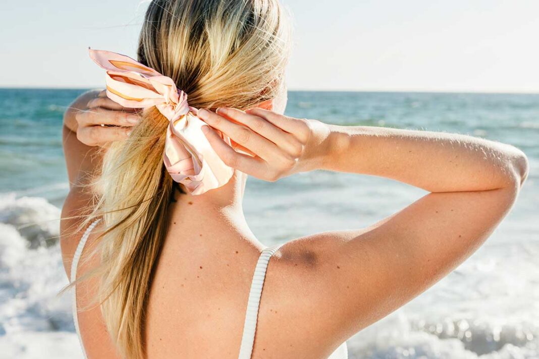 djevojka na plaži gleda u more i veže ružičastu mašnu na kosu