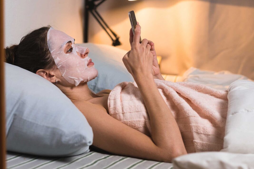 maska-za-lice Djevojka s maskom za lice leži i gleda mobitel