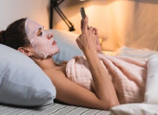 Djevojka s maskom za lice leži i gleda mobitel