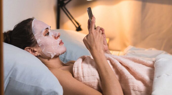 Djevojka s maskom za lice leži i gleda mobitel