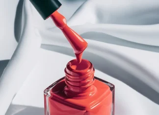 Crveni a lak za nokte kapa s kista u bocicu na bijeloj tekstilnoj pozadini