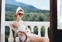 Djevojka sjedi u ogrtacu sa suncanim naocalama na balkonu