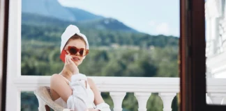 Djevojka sjedi u ogrtacu sa suncanim naocalama na balkonu