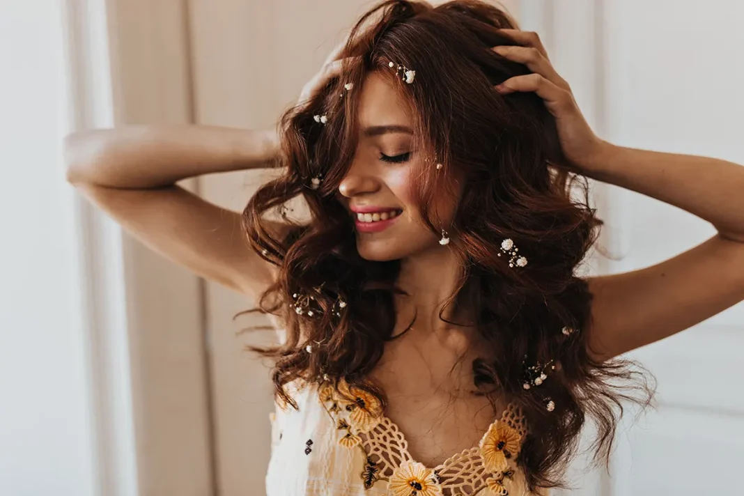 woman-stylish-yellow-top-ruffles-her-curly-hair-smiles-sweetly-against-white-doors Djevojka sa suhim cvijecem u kosi pozira pokraj prozira